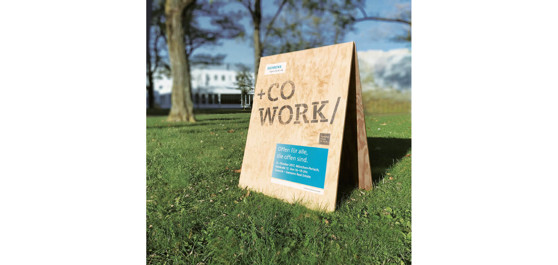Holzaufsteller auf grüner Wiese mit der Beschriftung +COWORK/ für das Coworking von Siemens
