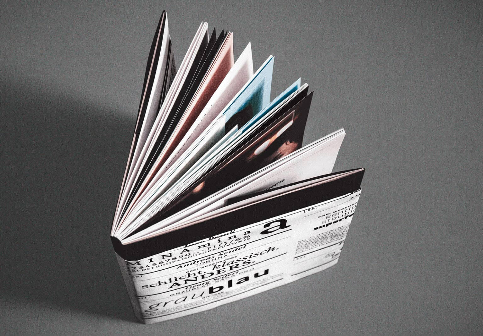 Das Buch der Typografischen Gesellschaft München steht aufgestellt und aufgefächert auf grauem Hintergrund