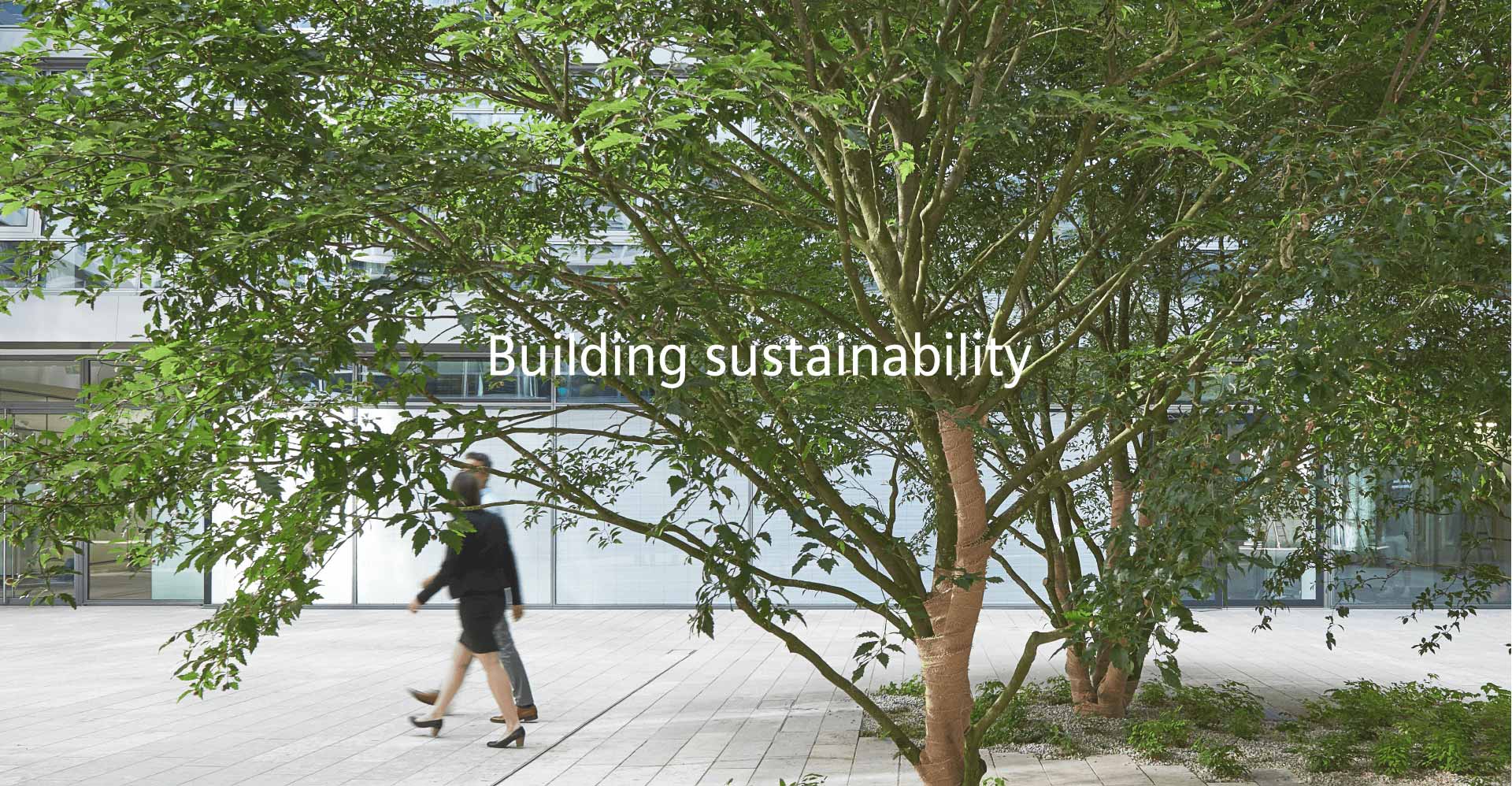 Menschen die an einem Gebäude mit Bäumen vorbei laufen mir dem Schriftzug Building sustainability