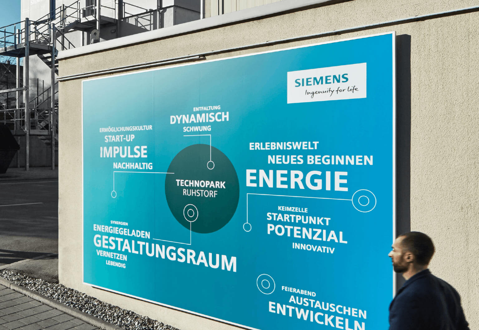 Billboard auf dem die Markenwerte von dem Siemens Technopark Ruhstorf erklärt werden ein Mann läft vorbei