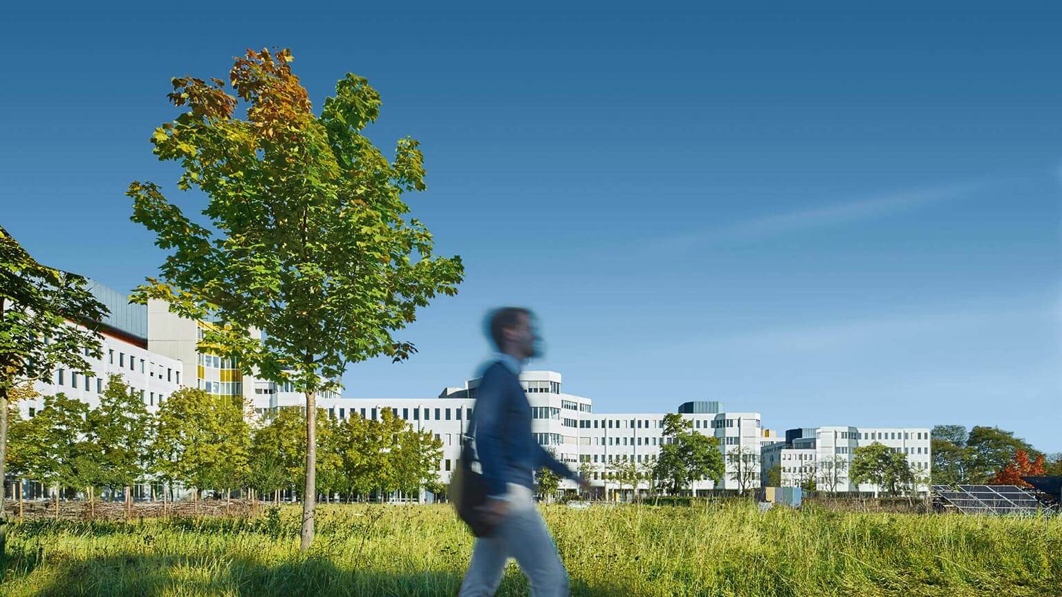 Mann läuft vor einem großen weißen Gebäude mit viel grün aus Bäumen und Wiese