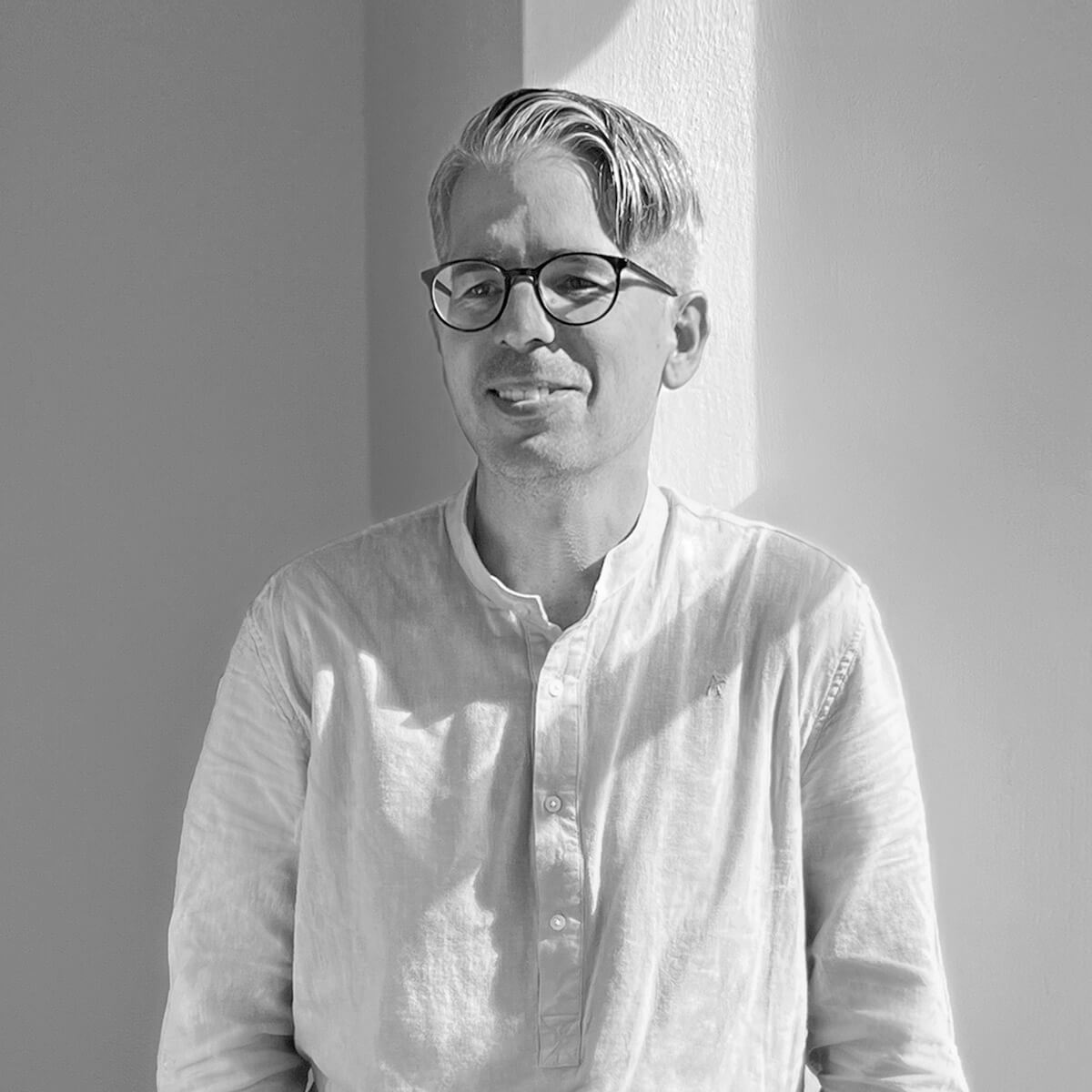 haefelinger design Mitarbeiter Thomas Tscherter lacht und steht vor einer weißen Wand als schwarzweiß Foto