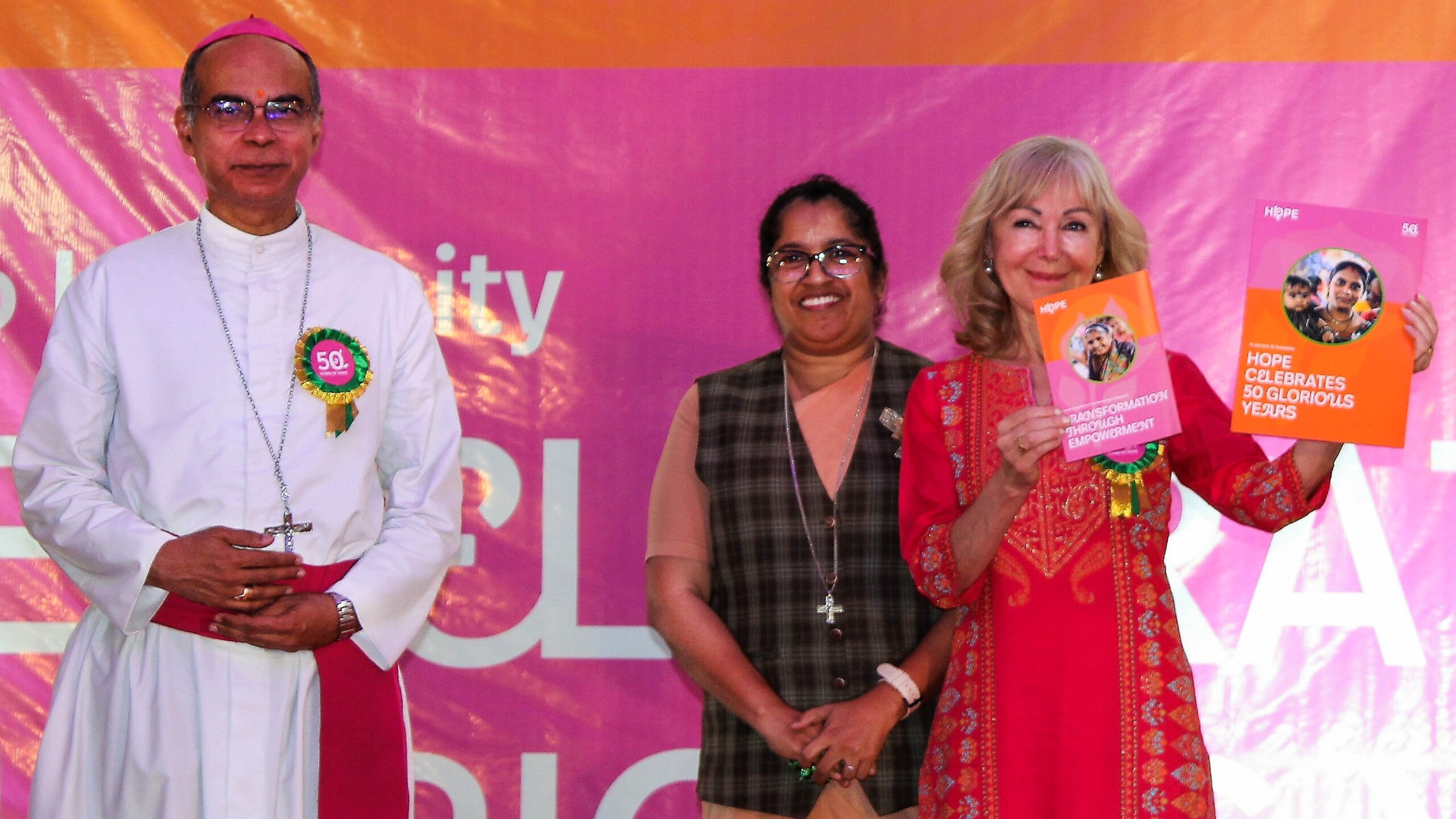 Gruppenfoto von dem Bischof von Pune und zwei Ehrenamtlichen Frauen von HOPE. Die eine hält zwei Broschüren für den Markenrelaunch von HOPE, Human Organisation for Pioneering in Education in die Kamera.
