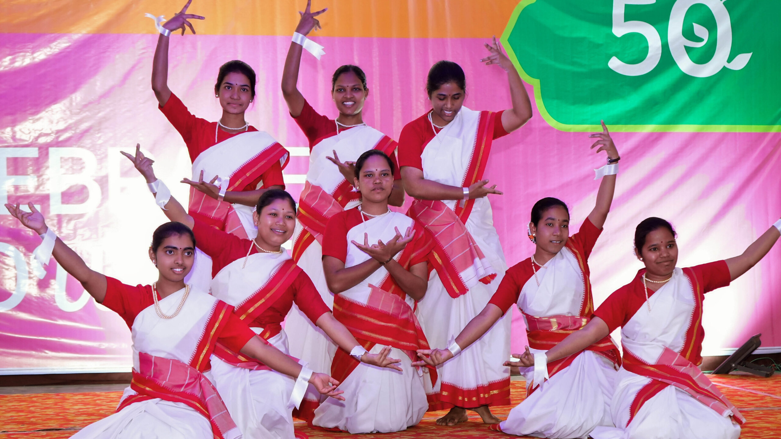 Gruppenfoto von den Tänzerinnen der Jubiläums Zeremonie mit Jubiläums-Banner von HOPE, Human Organisation for Pioneering in Education im Hintergrund.